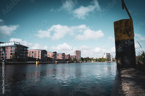 River landscape with modern buildings and a striking, yellow, graffiti-covered pillar, view from the traffic jam over the Hunte in 26122 Oldenburg, Germany
