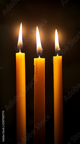 Candles with glowing flames burn brightly in the dark to cast a warm and inviting light that highlights the texture of the melting wax.