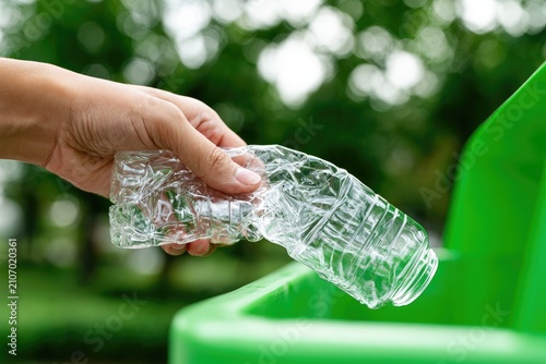 Hand holding crushed plastic bottle to discard into green bin