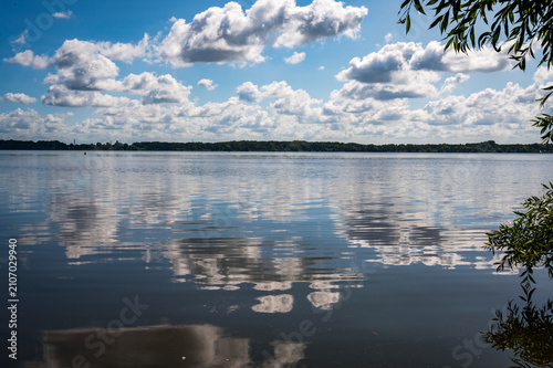 Clear blue lake surface with white clouds reflected in the calm water, surrounded by green trees, the view of Zwischenahner Meer, 26160 Bad Zwischenahn, Germany