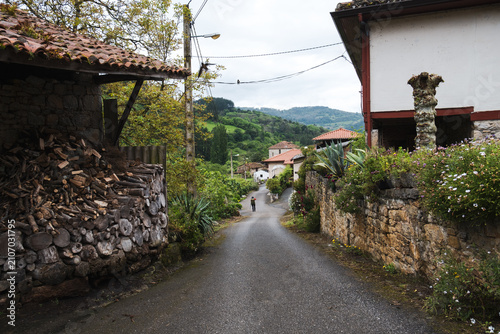Narrow asphalt street winding through a traditional rural village with stone houses on the Camino Primitivo.