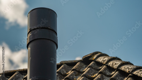 Black metal chimney pipe on weathered roof against blue sky