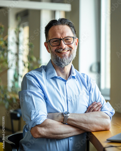 Cuadro en lienzo Mature businessman smiling confidently with arms crossed in modern office