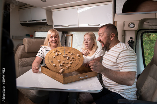 A family of three is playing a board game while sitting in a motorhome