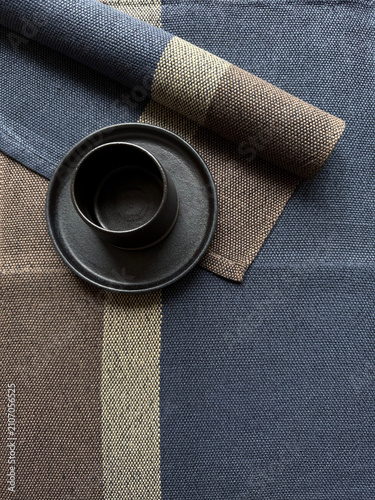 Rolled linen napkin and black ceramic cup in a minimalist composition. Handmade stoneware tableware with natural textile texture for home decor, dining, and sustainable lifestyle concepts.