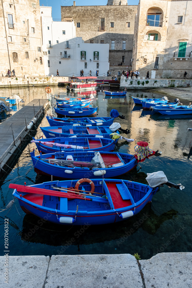 Fototapeta premium Monopoli, Italy - March 9, 2025: Ancient port (Porto antico) with moored blue boats. 15th century Gate of the ancient port leads from the city to the harbor