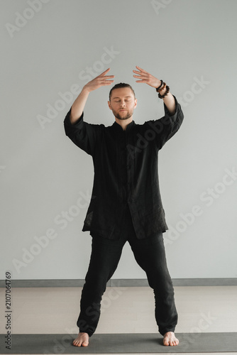 A man in black kimano practicing qigong energy exercises indoors