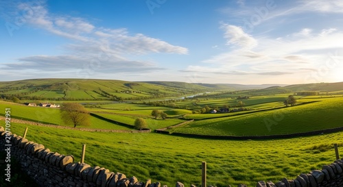 Panoramic view of lush green countryside with stone walls and rolling hills under bright summer sky.