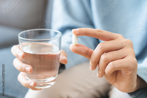 Sick, asian young woman, girl hand holding pill, painkiller medicine from stomach pain, headache, pain for treatment, take drug or vitamin and glass of water at home, pharmacy and health care concept.