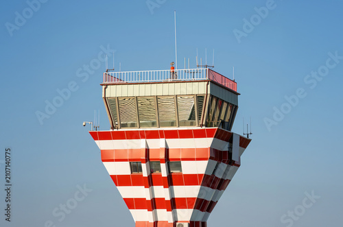 Red and white striped air traffic control tower against a clear blue sky