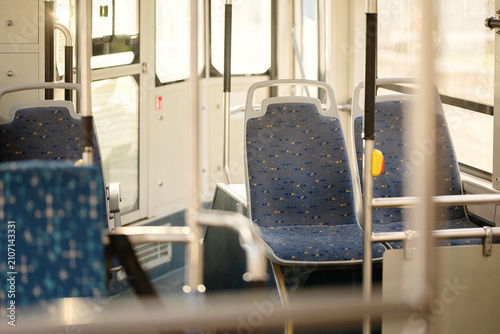Interior view of empty public transport vehicle with blue fabric seats handrails and large windows for urban transit concepts.