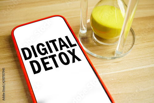 Smartphone displaying the words Digital Detox beside an hourglass on a wooden table. Concept of reducing screen time, mindfulness, mental wellness and healthy digital habits.