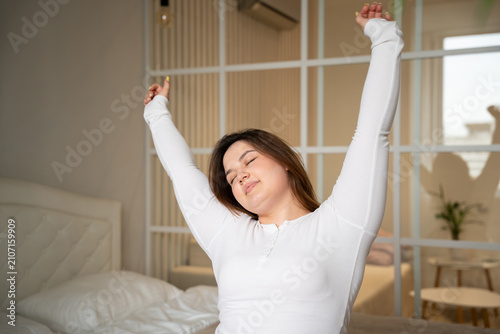 Foto Young woman stretching with closed eyes in bright bedroom during morning routine