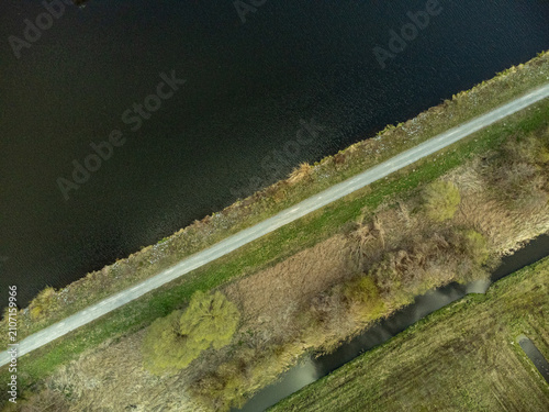 Obraz na plátně Aerial top down view of a gravel path on a dike dividing dark water and green landscape