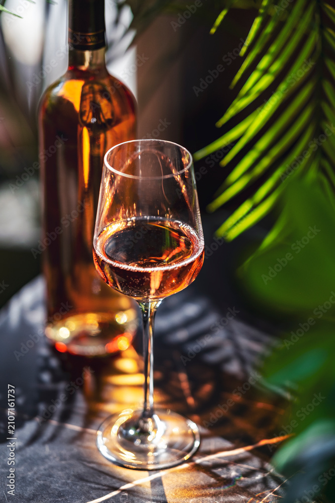 Obraz premium Blush rose wine glass standing on dark tabletop. Exotic resort lounge bar atmosphere and premium hotel catering hospitality concept.