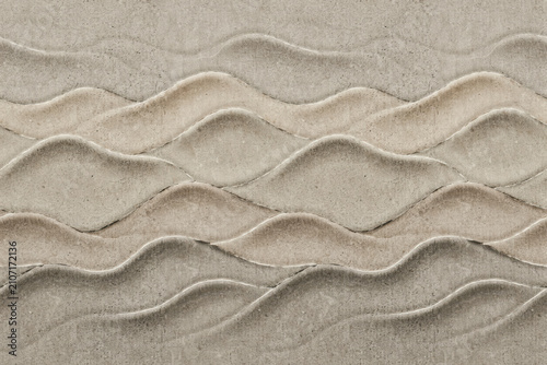 Textured sand surface with repeating wave patterns carved into the gritty creating a natural landscape effect in beige tones