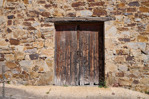 Old weathered wooden door standing in rustic stone wall