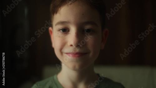 Close up portrait of a smiling 10 year old boy looking directly at the camera indoors. Natural light highlights freckles, genuine expression, childhood innocence and confidence.