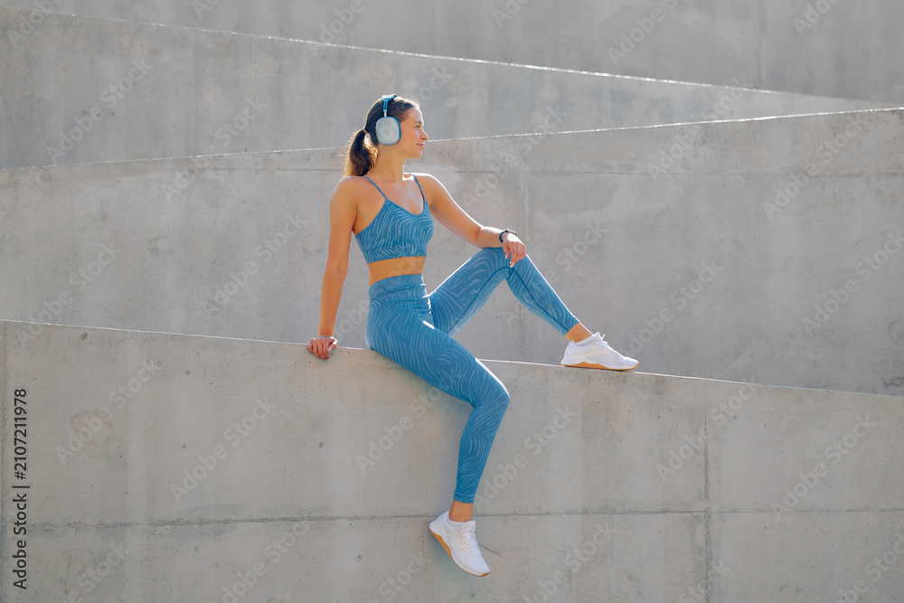 Fototapeta premium Sporty woman enjoys outdoor workout while sitting on a concrete structure in fitness gear
