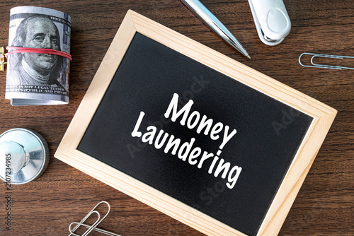 Money Laundering text on black chalkboard with dollar bills and office supplies on wooden desk, financial crime concept