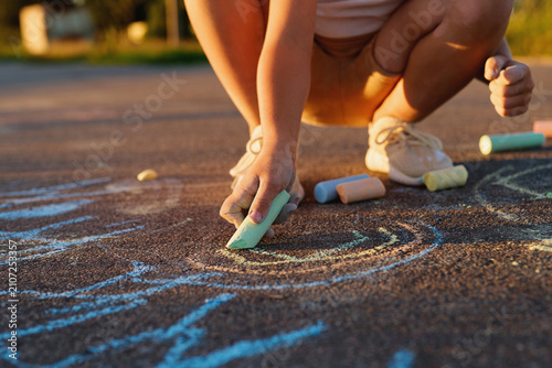 Fotografía A child crouches on a warm pavement using colorful chalk to create drawings in the afternoon sun
