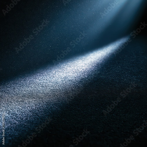 Abstract background with a diagonal beam of light hitting a textured surface, creating a dramatic spotlight effect with particles in a dark, moody atmosphere