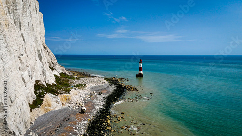 Obraz na płótnie Aerial drone view of Beachy Head Lighthouse standing beneath the iconic white chalk cliffs along the English Channel near Eastbourne, England, with calm turquoise waters and dramatic coastal scenery