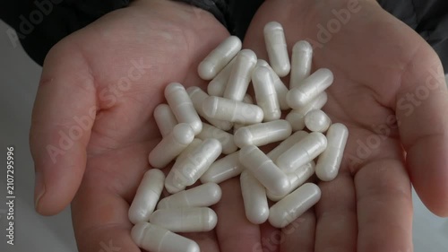 Close-up of human cupped hands holding a large pile of white medical capsules, showcasing healthcare, supplements, and wellness treatment.