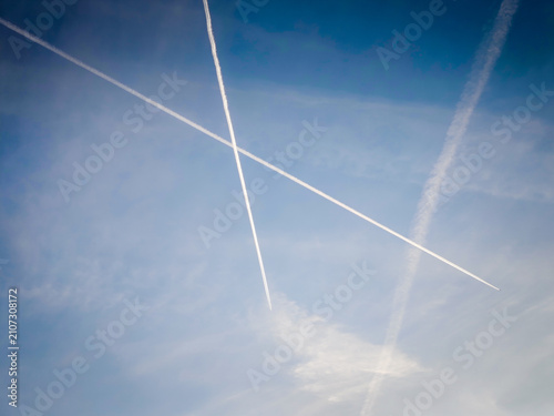 Bild auf Leinwand Airplane contrails crossing a clear blue sky, white vapor trails creating an abs