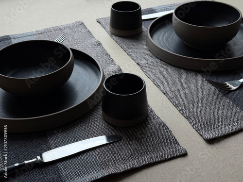 Modern black ceramic dinnerware arranged with cutlery on natural linen textile. Minimal dining composition with neutral tones, suitable for hospitality, home decor and lifestyle concepts.