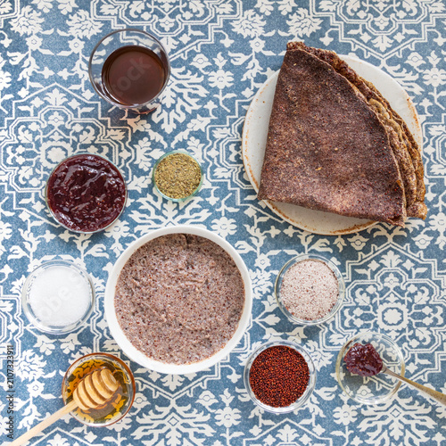 Close-up of pancakes and a dessert made with ragi (finger millet), featuring small bowls containing whole ragi and ragi ground into flour, along with a few ingredients to accompany the pancakes