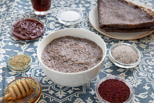 Close-up of pancakes and a dessert made with ragi (finger millet), featuring small bowls containing whole ragi and ragi ground into flour, along with a few ingredients to accompany the pancakes