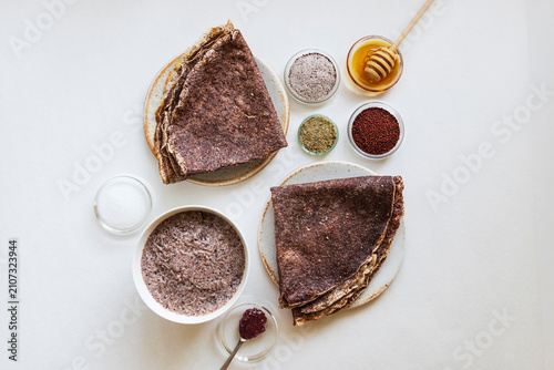Close-up of pancakes and a dessert made with ragi (finger millet), featuring small bowls containing whole ragi and ragi ground into flour, along with a few ingredients to accompany the pancakes