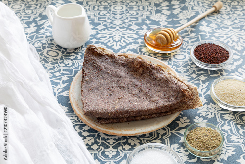 Close-up of ragi-based crepes (made from finger millet), with small bowls containing whole ragi and ragi ground into flour, along with a few ingredients served alongside the crepes