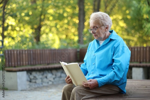 Obraz na płótnie Elderly woman reading book on bench in park, space for text