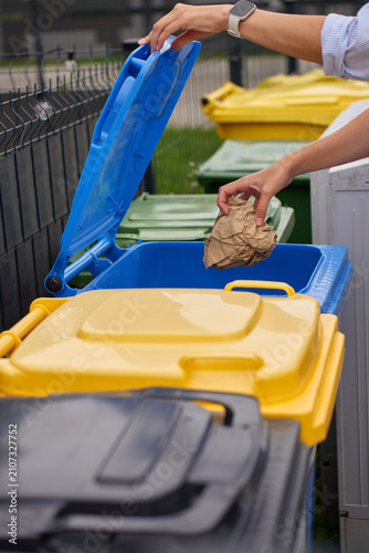 Obraz na plátně Hand throwing paper waste into blue recycling bin for proper waste sorting