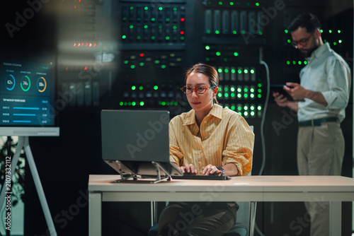 It engineer woman working on laptop in modern data center, managing server operations and cloud computing infrastructure