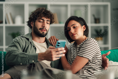 Young couple bonding and sharing content on a smartphone  connecting digitally at home on the sofa