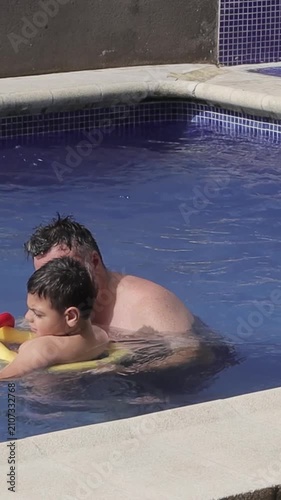 Father supporting son with cerebral palsy during swimming pool therapy