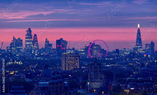 Panoramic view of the London skyline during the early morning blue hour, featuring the illuminated London Eye, The Shard, modern skyscrapers, historic architecture, and glowing city streets beneath a 
