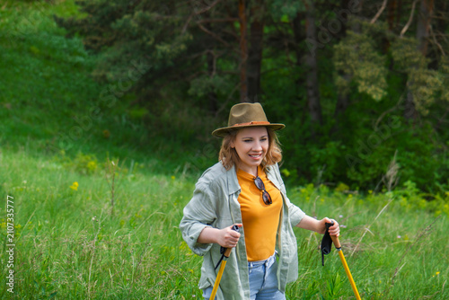 Foto Active woman hiking on green meadow trail with trekking poles wearing hat and casual shirt