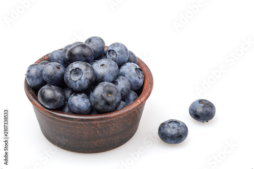 Ripe organic blueberries in a brown ceramic bowl with two berries outside, copy space.