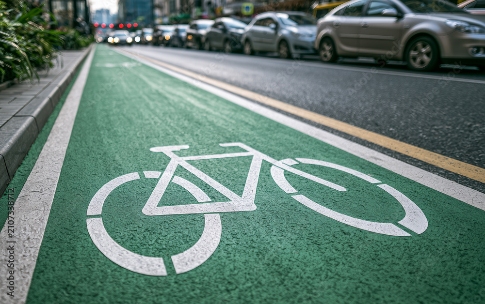 Obraz premium Vibrant green urban bicycle lane with a white painted bike symbol, alongside a busy street with blurred cars and greenery