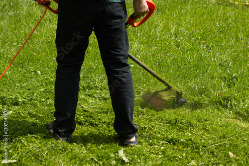 Person cutting grass with string trimmer on sunny day