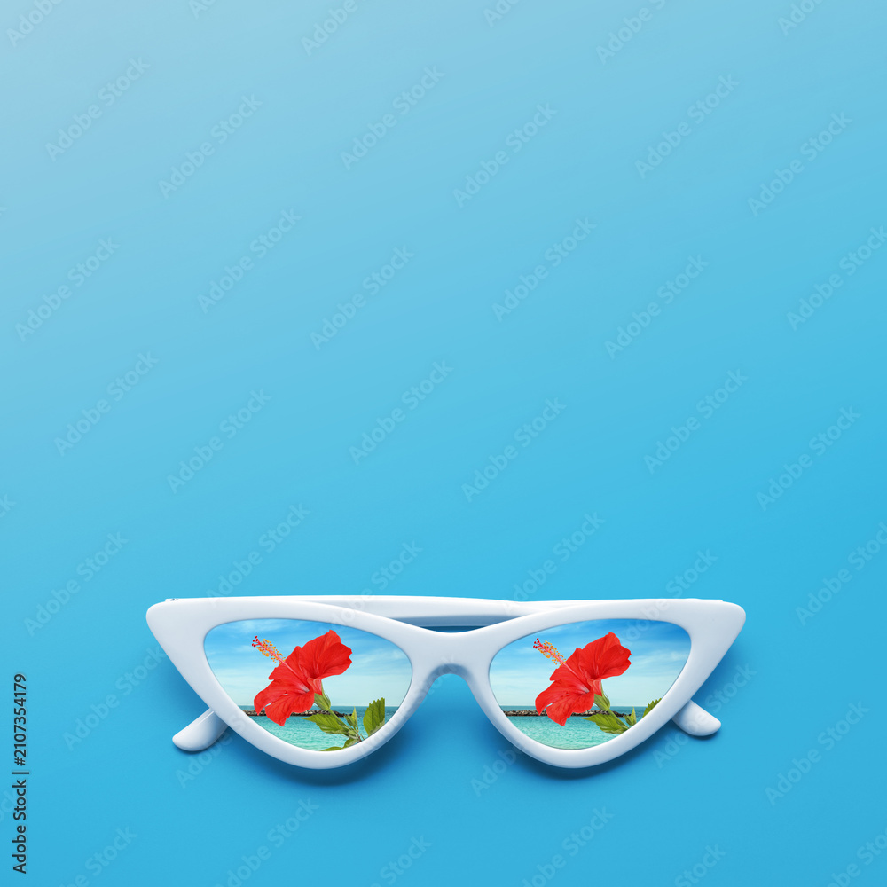Obraz premium Sunglasses reflecting hibiscus flower by sea on light blue background. Space for text