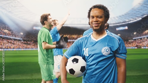 Photos Football player in a blue jersey holds a ball on the pitch and stands ready to play before the game as teammates prepare for the match nearby