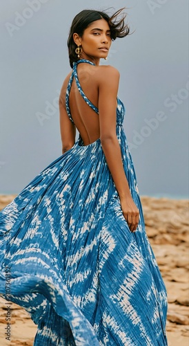 Stunning Indian woman wearing a flowing blue tie-dye maxi dress on a rocky beach