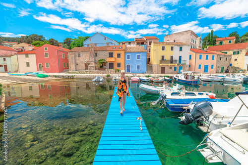 Woman enjoying a summer day, walking on a vibrant blue boardwalk in Luka Rovenska harbor surrounded by colorful traditional houses and boats on Losinj Island, Croatia