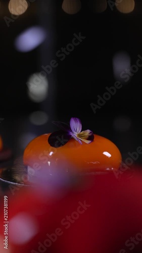 Close up of a beautifully crafted orange mousse pastry featuring a shiny mirror glaze in a professional kitchen, cinematic food videography
