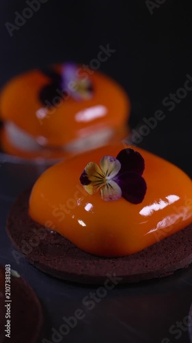 Close up of a beautifully crafted orange mousse pastry featuring a shiny mirror glaze in a professional kitchen, cinematic food videography
